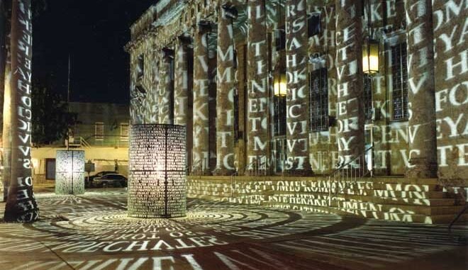Letras de luz projetadas sobre a fachada colunada de um edifício à noite — informação sobreposta à matéria