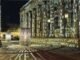 Letras de luz projetadas sobre a fachada colunada de um edifício à noite — informação sobreposta à matéria